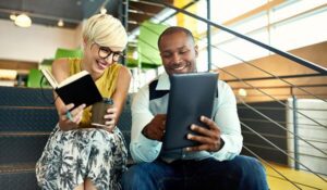 Two business colleagues, a man and woman, sitting on steps in a colourful office and looking at their notes.