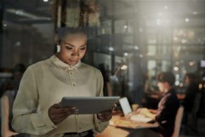 Woman working on tablet in a darkened room with colleagues working in the background for tech hiring agency in dubai