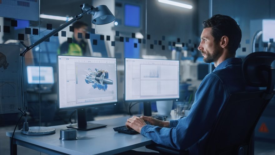 A digital designer working on a project on two computers in an office.